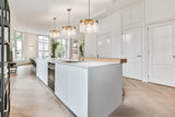Modern white kitchen island with built-in oven, sink, gold fixtures, and three crystal pendant lights