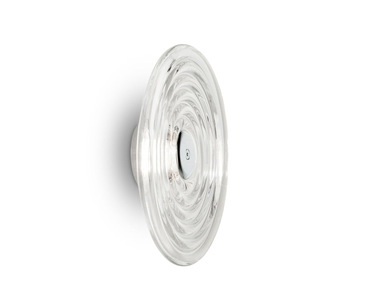 Clear glass wall sconce with concentric circular design mounted on white wall