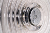Close-up of a shiny metallic drain stopper with water droplets inside a textured glass basin