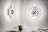 Modern circular glass wall lights creating ripple effects on white walls with silver candle and foam on marble surface